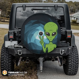 May include: A black Jeep with a spare tire cover featuring a green alien with a peace sign. The alien is on a blue and green swirling background.