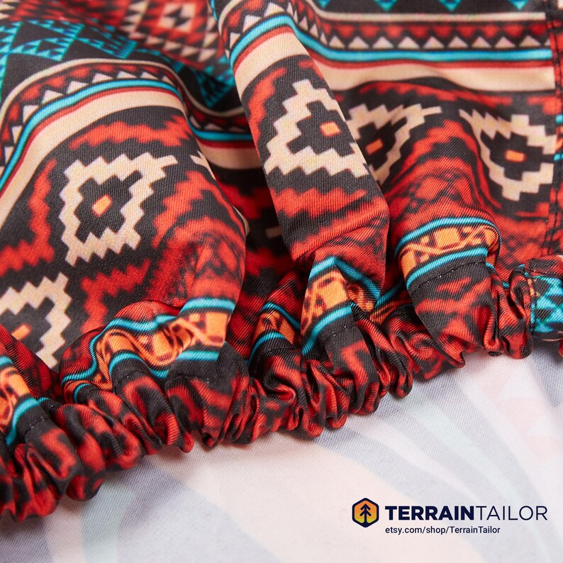 May include: Close-up of a fabric with a Southwestern-inspired pattern. The design features geometric shapes in red, black, tan, and turquoise. The fabric is gathered at the edge, creating a ruffled effect. The Terrain Tailor logo is visible.