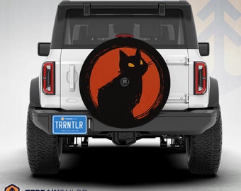 May include: A white SUV with a black cat silhouette on a red circle spare tyre cover. The number plate reads "TRRNTLR".