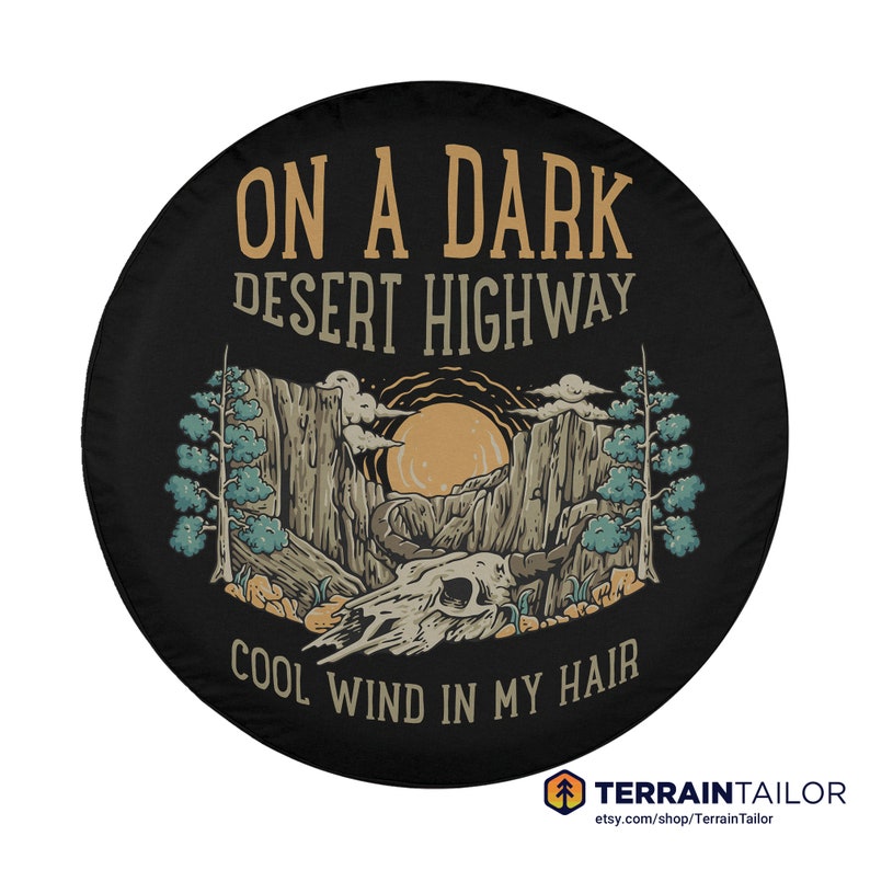 May include: Black spare tire cover with a desert landscape design. The cover features a mountain scene with a setting sun, a skull, and text that reads "ON A DARK DESERT HIGHWAY COOL WIND IN MY HAIR". The Terrain Tailor logo is at the bottom.