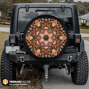 Puede incluir: Un Jeep negro con una cubierta de rueda de repuesto que presenta un diseño de mandala colorido con acentos naranja, amarillo y morado. El mandala está sobre un fondo negro.