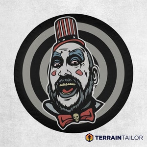 May include: A black and white illustration of a creepy clown with a red, white, and blue hat. The clown is smiling with a wide, toothy grin. The background is a black and white target pattern.