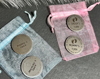 May include: Three silver coins with the text "New Parent Decision Coin" and a baby footprint. The coins have the text "Daddy's Turn", "Mummy's Turn", and "Mummy's Turn" on them. The coins are in small bags, one blue, one pink, and one white.