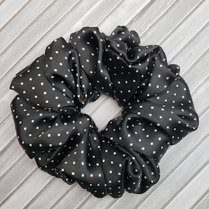 Peut inclure: Un chouchou en satin noir orné de pois blancs. Cet accessoire pour cheveux est fabriqué à partir d'un tissu froncé et est conçu pour maintenir les cheveux. Un accessoire de coiffure élégant et fonctionnel.