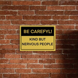 以下が含まれることがあります： レンガの壁に「BE CAREFYL! KIND BUT NERVOUS PEOPLE」と書かれた金色と黒色の看板