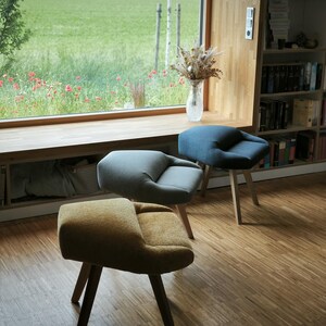 May include: Three modern accent chairs with wooden legs and curved, upholstered seats in mustard yellow, gray, and blue. The chairs are arranged in a room with a large window overlooking a green field.