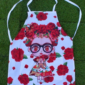 May include: White apron featuring a cartoon illustration of a woman with a floral headdress, glasses, and a monkey. The apron is decorated with red roses and has a front pocket and white ties.