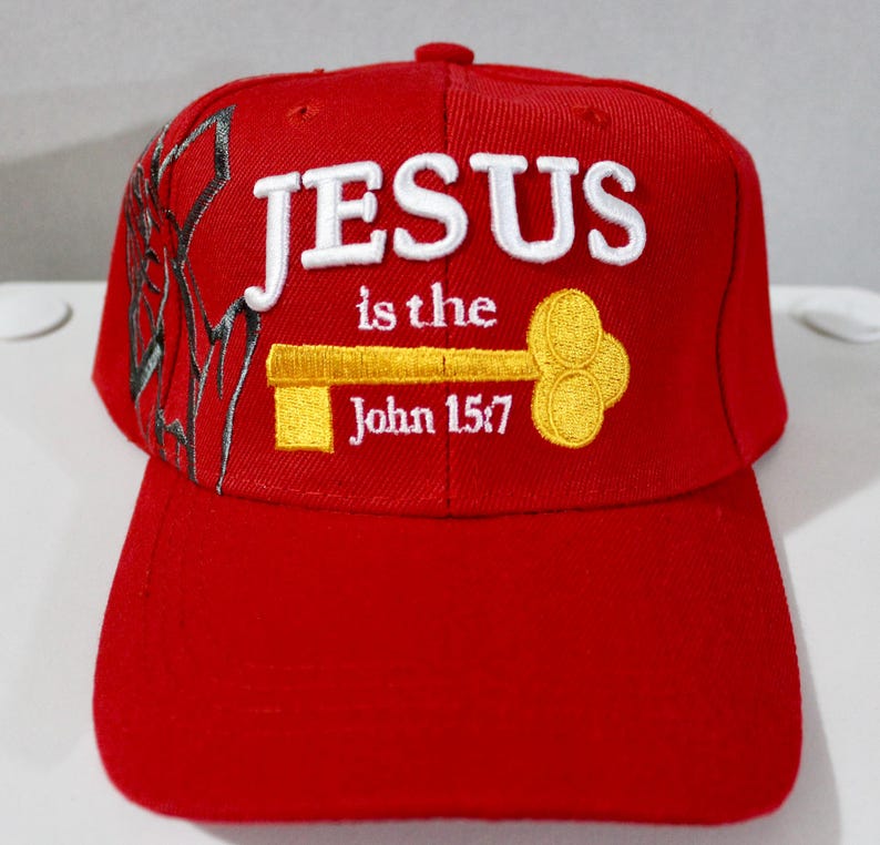 May include: A red baseball cap with the words "JESUS is the" and "John 15:7" embroidered in white and yellow. The cap features a key design and a decorative pattern on the side.