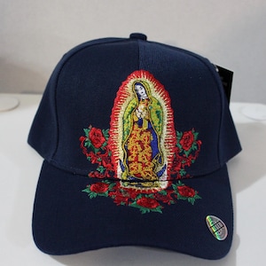 May include: A navy blue baseball cap with an embroidered image of the Virgin Mary surrounded by red roses. The cap has a curved brim and an adjustable strap.