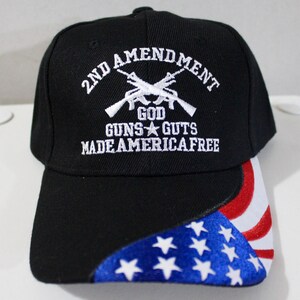 Peut inclure: Casquette de baseball noire avec texte brodé blanc : "2ND AMENDMENT GOD GUNS GUTS MADE AMERICA FREE" et fusils croisés. La visière présente un motif du drapeau américain avec des étoiles bleues et des rayures rouges et blanches.