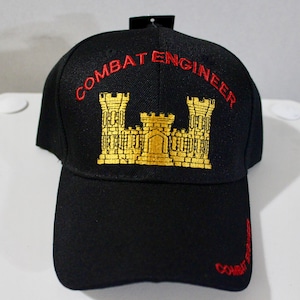 May include: Black baseball cap with "COMBAT ENGINEER" embroidered in red, arched across the front. A gold emblem of a castle is centered below the text. The words "COMBAT ENGINEER" are also embroidered on the brim.