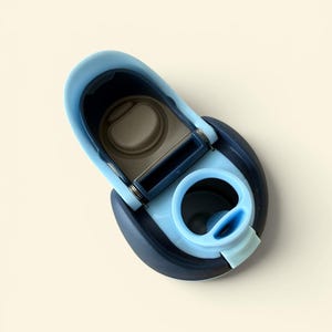 May include: A close-up of a blue and navy water bottle lid. The lid is open, revealing the interior. The lid has a light blue spout and a dark blue base. The lid is made of plastic.