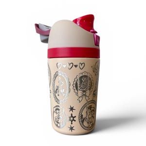 May include: A beige water bottle with a red lid and accents. The bottle features silver illustrations of cartoon characters and symbols. The top has a flip-top opening and a gray handle. The bottle is designed for cold beverages.
