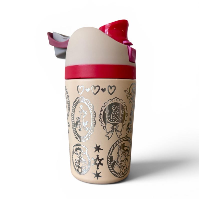 May include: A beige water bottle with a red lid and accents. The bottle features silver illustrations of cartoon characters and symbols. The top has a flip-top opening and a gray handle. The bottle is designed for cold beverages.