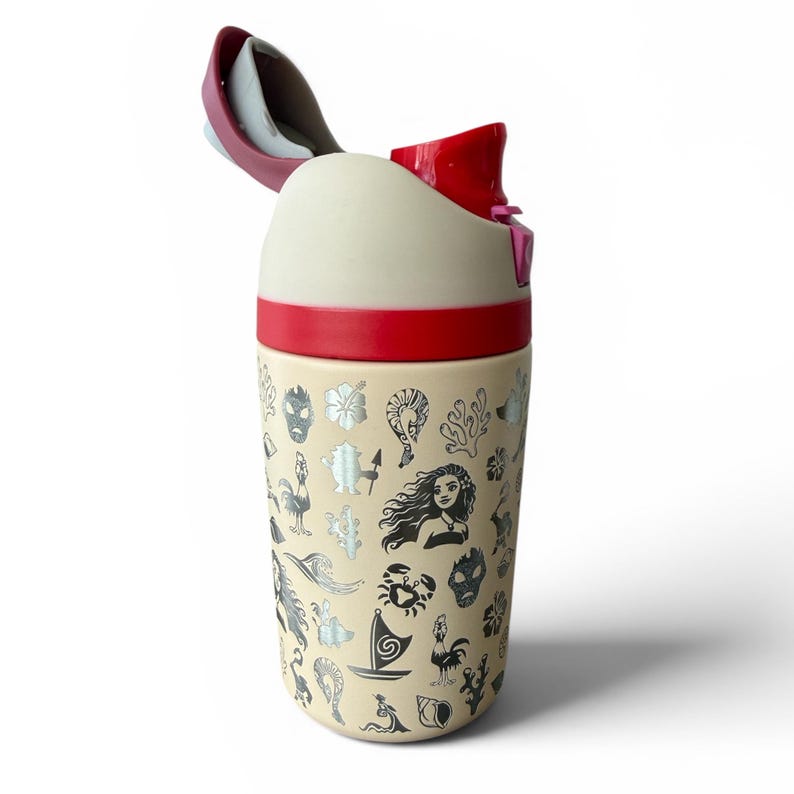 May include: A cream-colored travel mug with a red lid and accents. The mug is decorated with various black and silver illustrations, including flowers, faces, and sea creatures. The lid is open, revealing a white interior.