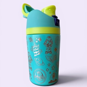 May include: A teal water bottle with a flip-top lid, featuring a yellow accent and a silver design of characters and symbols from the movie Toy Story. The bottle has a cylindrical shape and is designed for easy handling.