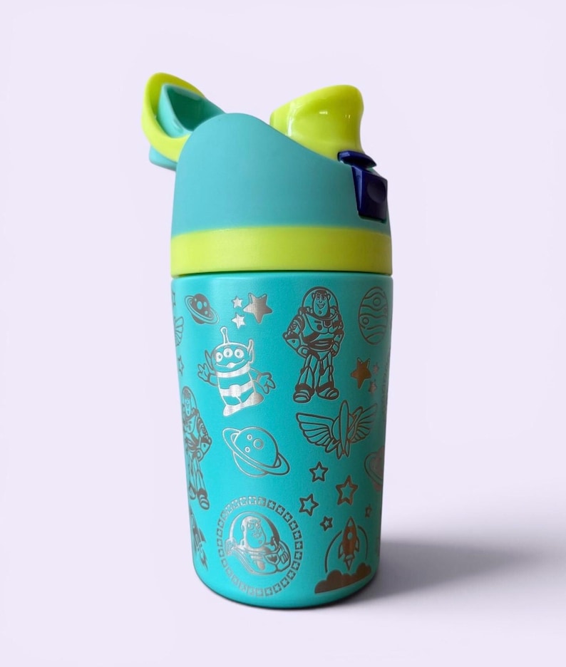 May include: A teal water bottle with a flip-top lid, featuring a yellow accent and a silver design of characters and symbols from the movie Toy Story. The bottle has a cylindrical shape and is designed for easy handling.