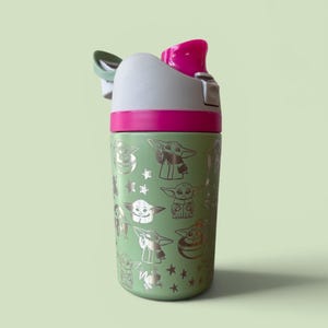 May include: A light green water bottle featuring a repeating silver metallic pattern of a small creature with large ears and eyes, interspersed with stars. The bottle has a grey and bright pink lid with a flip-top mechanism and a green carry loop.