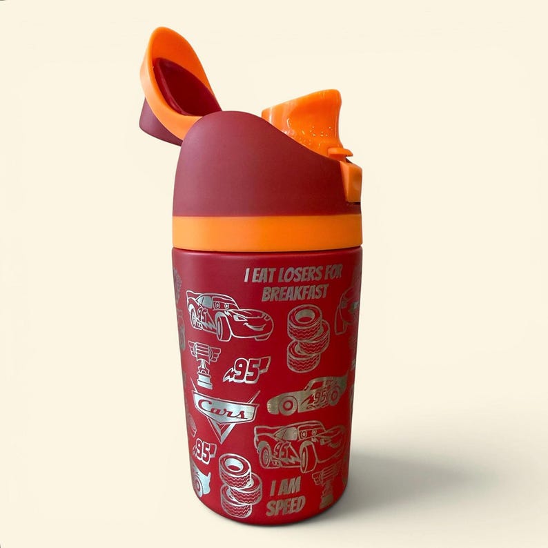 May include: A red and orange water bottle with a flip-top lid. The bottle features illustrations of race cars and the text "I EAT LOSERS FOR BREAKFAST" and "I AM SPEED".