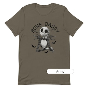 Puede incluir: Una camiseta verde con una ilustraci&oacute;n en blanco y negro de un personaje esqueleto con el texto "Bone Daddy" encima. La camiseta est&aacute; disponible en verde militar.