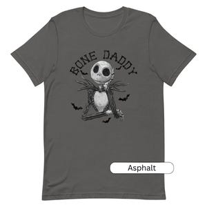 Puede incluir: Una camiseta gris oscuro con una ilustraci&oacute;n en blanco y negro de Jack Skellington de Pesadilla antes de Navidad. El texto "Bone Daddy" est&aacute; impreso sobre la ilustraci&oacute;n. La camiseta est&aacute; disponible en el color Asfalto.