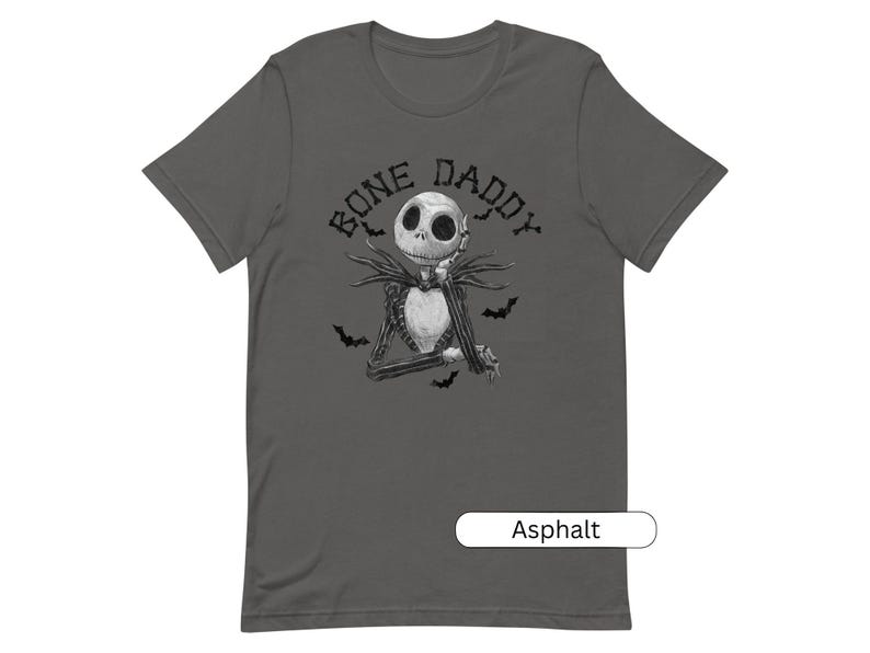 Puede incluir: Una camiseta gris oscuro con una ilustraci&oacute;n en blanco y negro de Jack Skellington de Pesadilla antes de Navidad. El texto "Bone Daddy" est&aacute; impreso sobre la ilustraci&oacute;n. La camiseta est&aacute; disponible en el color Asfalto.