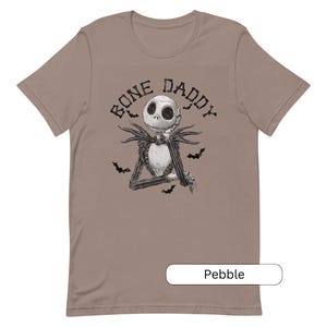 Puede incluir: Una camiseta de color marr&oacute;n claro con una ilustraci&oacute;n en blanco y negro de Jack Skellington de Pesadilla antes de Navidad. El texto "Bone Daddy" est&aacute; impreso en negro sobre la ilustraci&oacute;n.