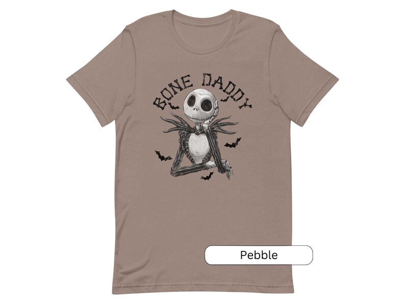 Puede incluir: Una camiseta de color marr&oacute;n claro con una ilustraci&oacute;n en blanco y negro de Jack Skellington de Pesadilla antes de Navidad. El texto "Bone Daddy" est&aacute; impreso en negro sobre la ilustraci&oacute;n.