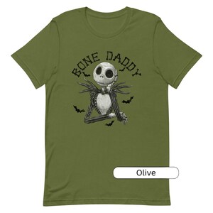 Puede incluir: Camiseta verde oliva con una ilustraci&oacute;n en blanco y negro de Jack Skellington de Pesadilla antes de Navidad. El texto "Bone Daddy" est&aacute; impreso en negro sobre la ilustraci&oacute;n.