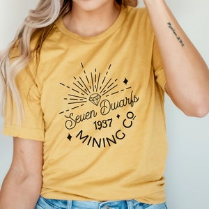 May include: A yellow t-shirt with a black graphic design of a diamond, sunburst, and the text "Seven Dwarfs 1937 Mining Co."