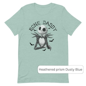 Puede incluir: Una camiseta azul claro con una ilustraci&oacute;n en blanco y negro de Jack Skellington de Pesadilla antes de Navidad. El texto "Bone Daddy" est&aacute; impreso sobre la ilustraci&oacute;n.
