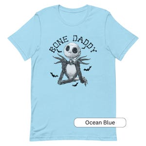 Puede incluir: Una camiseta azul claro con una ilustraci&oacute;n en blanco y negro de Jack Skellington de Pesadilla antes de Navidad. El texto "Bone Daddy" est&aacute; impreso sobre la ilustraci&oacute;n.