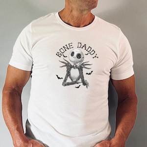 Puede incluir: Camiseta blanca con una ilustraci&oacute;n en blanco y negro de Jack Skellington de Pesadilla antes de Navidad. El texto "Bone Daddy" est&aacute; impreso sobre la ilustraci&oacute;n.