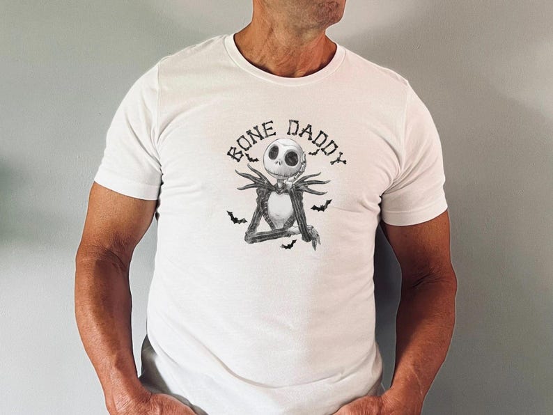 Puede incluir: Camiseta blanca con una ilustraci&oacute;n en blanco y negro de Jack Skellington de Pesadilla antes de Navidad. El texto "Bone Daddy" est&aacute; impreso sobre la ilustraci&oacute;n.