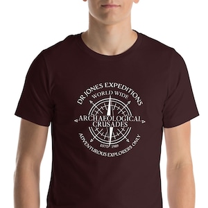 May include: A maroon t-shirt with a white compass design that says "Dr. Jones Expeditions World Wide Archaeological Crusades Est. 1989 Adventurous Explorers Only"