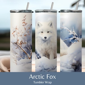 May include: Three stainless steel tumblers featuring a white arctic fox, a snowy forest scene, and a snowy branch design. The tumblers are displayed on a wooden surface with a white cloth napkin. The text "Arctic Fox Tumbler Wrap" is positioned below the tumblers.