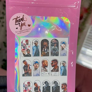 May include: A pink holographic resealable pouch containing a sheet of nail decals featuring various photographic portraits of a man. A circular white sticker on the pouch reads Thank You for supporting my small business with a small heart icon.