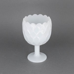 May include: White glass vase with a textured, scalloped design. The vase has a wide, round base and a tall, slender stem.