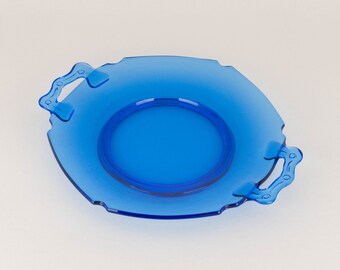 Op de afbeelding: Een transparant blauw serveerblad met twee handvatten. De lade heeft een cirkelvormige inkeping in het midden en een decoratieve rand. De handvatten hebben een uniek kettingontwerp. De lade is gemaakt van een helder, duurzaam materiaal.