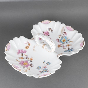 May include: A white porcelain serving dish with a handle. The dish is divided into two sections and features a floral design in pink, blue, and yellow.
