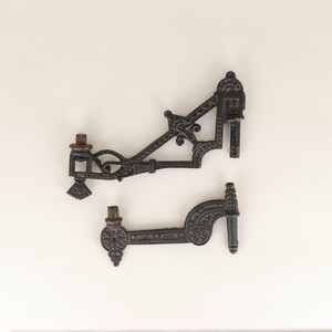 Puede incluir: Dos soportes de pared de hierro fundido negro con diseños intrincados. Los soportes son de metal y tienen un acabado oscuro.