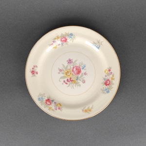 May include: A white ceramic plate with a gold rim and a floral design in shades of pink, yellow, and blue.