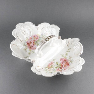 May include: A white porcelain serving dish with a handle. The dish is divided into two sections and features a floral design with pink roses and green leaves.