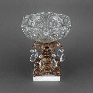 May include: A clear glass bowl with a decorative cut-glass design sits on a gold metal stand with crystal drop accents. The stand has a white marble base.