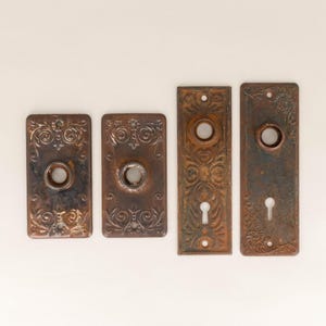 May include: Four antique door knobs with ornate designs and keyholes. The knobs are made of metal and have a brown patina.