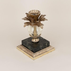 Puede incluir: Un candelero dorado en forma de piña con un globo de vidrio transparente y una base de mármol negro.