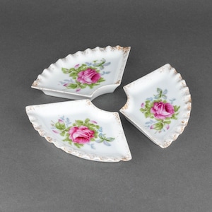 May include: Three white porcelain fan-shaped dishes with gold trim and pink rose floral designs.