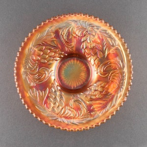 May include: A vintage iridescent glass plate with a scalloped edge and a raised design of pinecones and leaves. The plate is in shades of orange, red, and gold.
