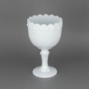 Puede incluir: Tazón blanco de vidrio de leche sobre un pedestal con un borde festoneado y un diseño de cuentas decorativas. El tazón está sobre una base de pedestal blanco.