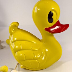 May include: A yellow rubber duck toy with a red beak and black eyes. The duck has a textured surface and is in a sitting position.